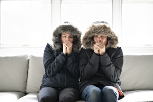 Cold couple in coats on couch-7 reasons to get a furnace tune-up-Allgeier Air-Louisville-300x200